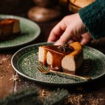 Ein Stück Salted Caramel Cheesecake mit Karamellsauce wird mit einer Hand auf einem gedeckten Tisch serviert.