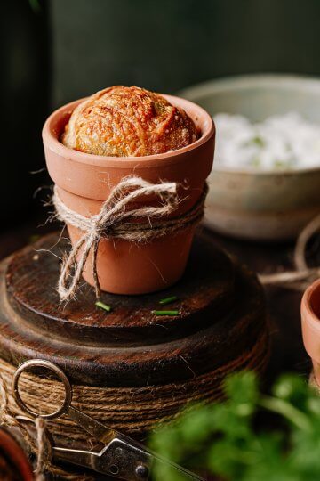 Joghurt-Käse-Sauerteigbrot im Tontöpfchen zwischen Schnittlauch sowie Petersilie und Kräuteraufstrich im Hintergrund.
