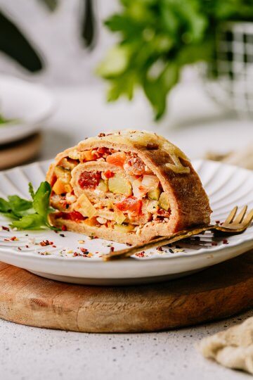 Pfannkuchen-Gemüse-Roulade aus dem Ofen auf einem Teller mit Petersilie angerichtet, in heller natürlicher Lichtstimmung